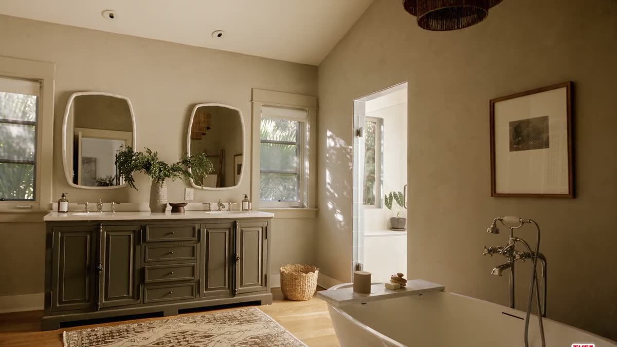 Camera gliding past the freestanding soaking tub and olive double vanity